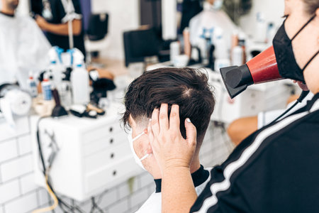 Hairdresser with mask drying the hair of a male with mask sitting in a salonの写真素材