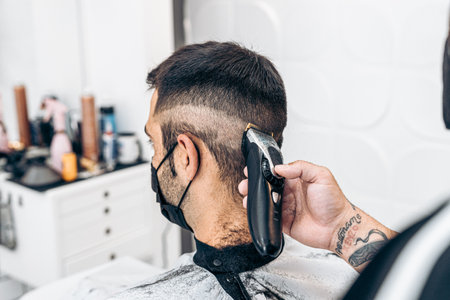 Barber shaving the back of the nape of a man with a mask in a barber shopの写真素材