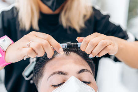 Hairdresser curling the hair of a client with a mask using an electric curlerの写真素材