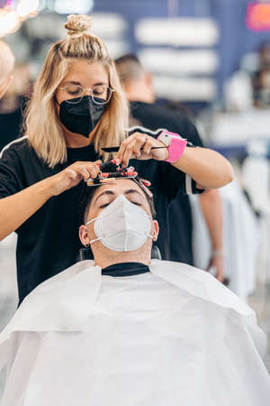 Vertical photo of a hairdresser adjusting curls of the hair of a man with maskの写真素材