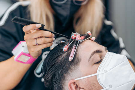 Hairdresser fixing curls of the hair of a man with mask using the pin of a combの写真素材