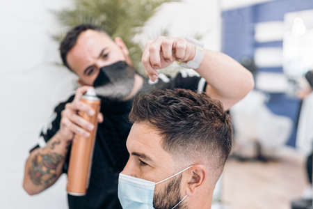 Barber putting hairspray on the hair of a masked manの写真素材