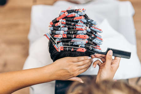 Hands of a hairdresser fixing the hair of a man with curlers using a combの写真素材