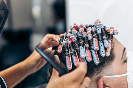 Close up view of a hairdresser fixing the hair of a man with curlers using a combの写真素材