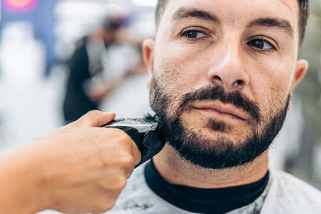 Close up view of a barber shaving a beard with an electric razor in a salonの写真素材