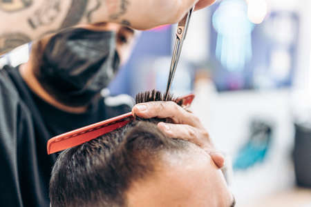 Barber with mask cutting the hair of a client in a barbers shopの写真素材