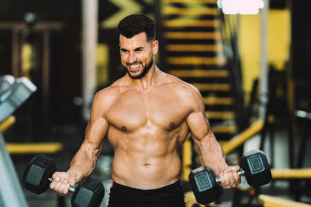 Man raising metallic dumbbells in a gym with expression of satisfactionの写真素材