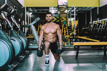 Smiling man doing squats with weights in a gymの写真素材