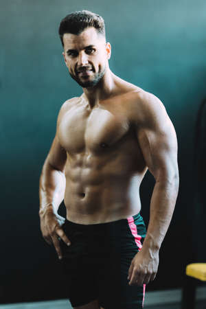 Vertical photo of an adult strong caucasian man posing in a gym