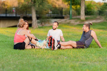 Group of friends sitting in a circle in a park with inline skatesの写真素材