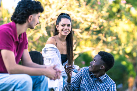Diverse young people sitting on a bench in park while talking in summer