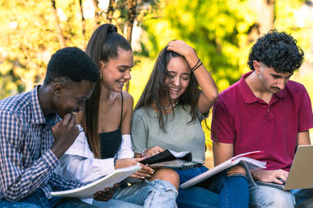 Group of diverse students reading notebooks and using a laptop sitting outdoorsの写真素材