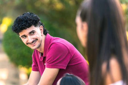 Man with modern hairstyle sitting on a bench while talking with other people