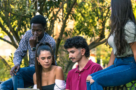 Group of multiethnic students using a laptop while sitting on a bench of a park