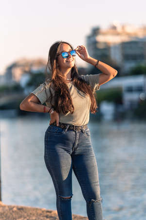 Young caucasian woman with sunglasses standing next to a river during sunsetの写真素材
