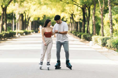 Young man helping to learn to skate to a woman in a public parkの写真素材
