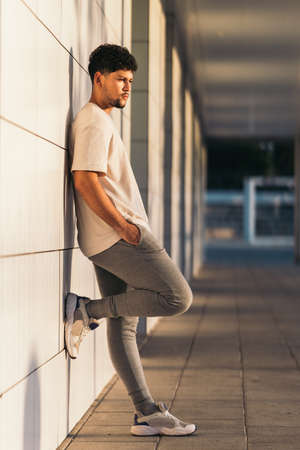 Vertical photo of a man leaning on the facade of a building during sunset