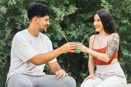 Two people toasting with soft drinks sitting in a parkの写真素材