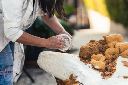 Woman spreading white paste from a pot on the surface of a polystyrene figureの写真素材