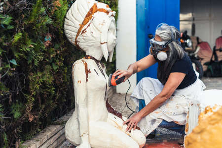 Woman with a mask filing a polystyrene sculpture with an electric polisherの写真素材