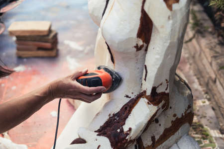 Hand of a woman using an electric polisher on a polystyrene figure outdoorsの写真素材