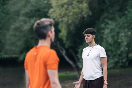 Men standing facing each other while doing yoga outdoorsの写真素材