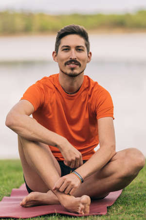 Sportive man with a lgtb rainbow bracelet sitting on a yoga mat in a park