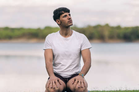 Athletic man sitting on a yoga mat with distracted expression next to a lakeの写真素材
