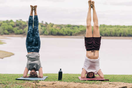 Two people with the head on the floor practising yoga in a park with a lakeの写真素材