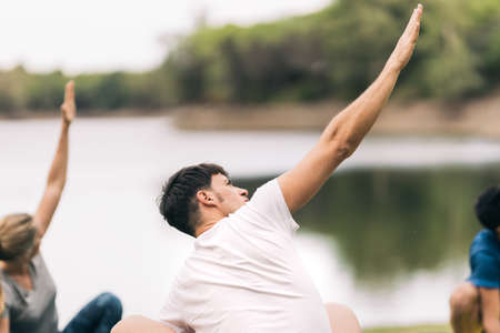 Man raising the arm while doing yoga with a group of people outdoors