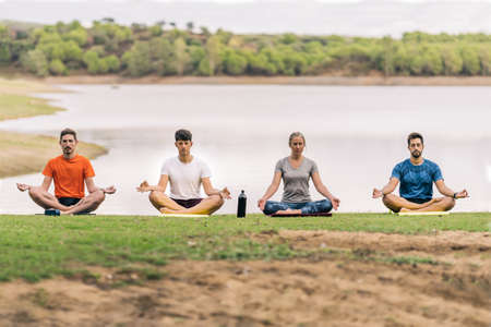 Four people sitting while doing the lotus position of yoga next to a lakeの写真素材