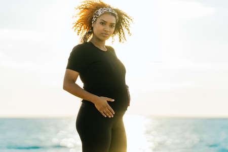 Rays of the sun illuminating a pregnant woman touching her belly on the beachの写真素材
