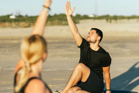 Man raisin arm while doing a yoga next to his coach on the beachの写真素材
