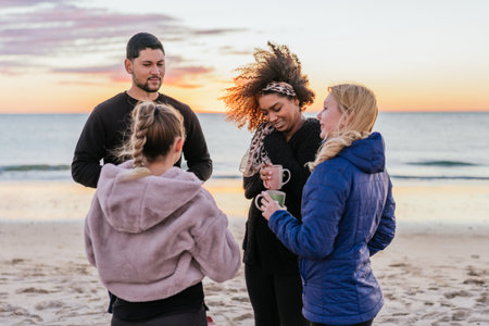 People with sportive clothes standing drinking tea on a beach during sunsetの写真素材