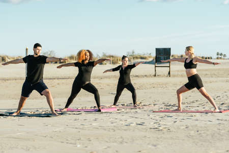 Yoga teacher conducting a class with multiethnic people on a beachの写真素材