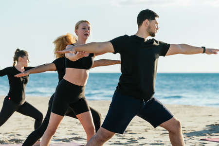 Yoga instructor correcting the pose of a man during a yoga class on a beachの写真素材
