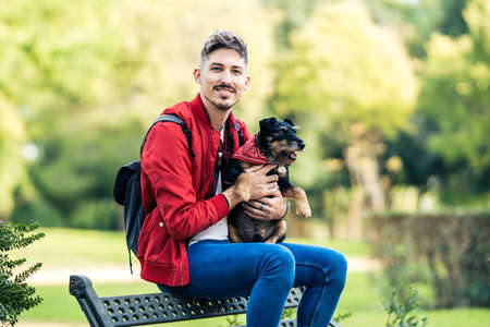Young man with a dog sitting on a bench while facing the camera