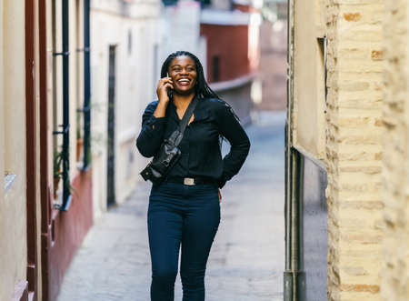 African woman walking on the street while talking to the mobile and smilingの写真素材