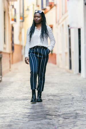 African woman with modern clothes walking distracted outdoorsの写真素材