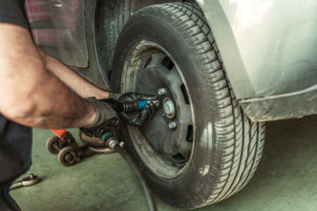 Man using an electric screwdriver to remove a wheel in a garageの写真素材