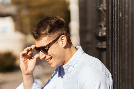 a smiling young man putting on a pair of sunglasses