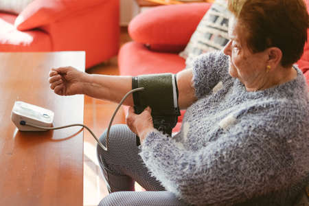 Elderly woman putting on the compression cuff of a blood pressure monitor.