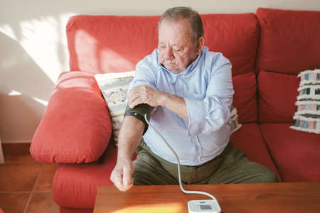 older man puts the cuff of the blood pressure monitor on his right armの写真素材