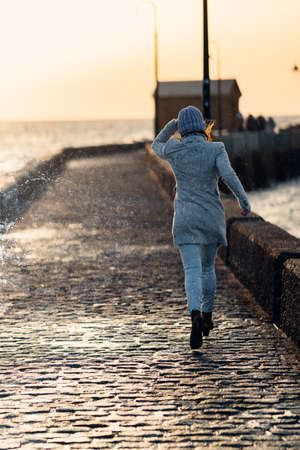 woman flees the water from a wave that has crashed against the promenade wallの写真素材