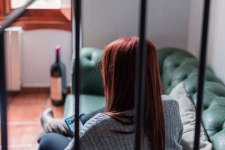 unrecognisable red-haired woman looks at her mobile phone sitting in an armchairの写真素材