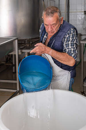 older man pouring water with a bucket into the plastic container to prepare the brine.
