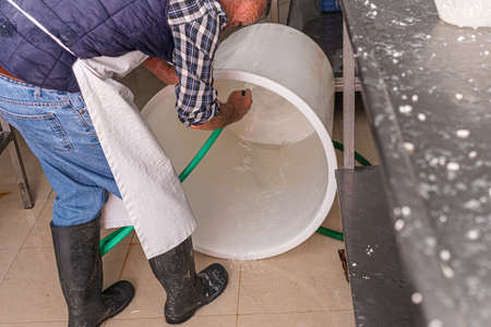 older man rinses the inside of the plastic container with a hose to prepare brine