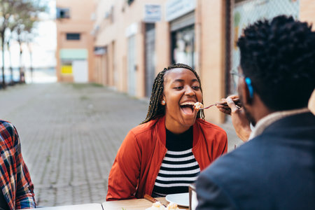 young black woman opening her mouth to eat food offered to her by her partnerの写真素材