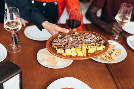 waiter serving a plate of barbecued meat with french friesの写真素材