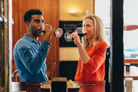 multiethnic couple look at each other with feeling while drinking red wine from their glasses